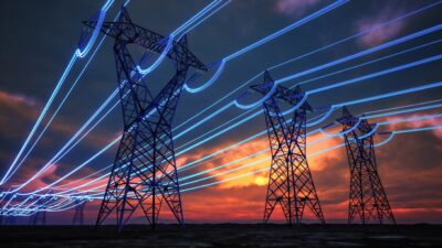 Imagem mostra torres de distribuição de energia elétrica ao por do sol.