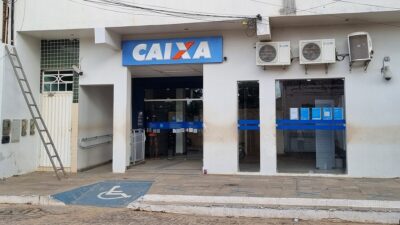 Agência da Caixa Econômica Federal com fachada branca, placa azul com a logomarca do banco, entrada acessível por rampa e portas de vidro voltadas para a rua.