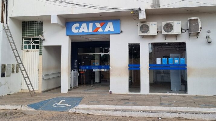 Agência da Caixa Econômica Federal com fachada branca, placa azul com a logomarca do banco, entrada acessível por rampa e portas de vidro voltadas para a rua.
