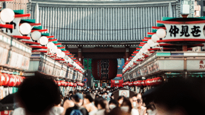 Uma rua lotada de pessoas e ladeada por lanternas japonesas; foto tirada de um plano acima das cabeças