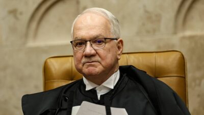 O presidente do STF, Edson Fachin, veste toga preta e está sentando em uma mesa, segurando papéis