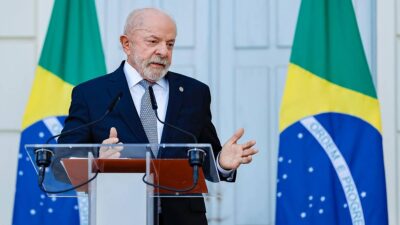 Presidente da República, Luiz Inácio Lula da Silva em pé, de frente a um púlpito, com bandeira do Brasil atrás.