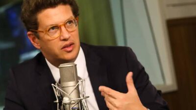 Ricardo Salles, ex-ministro do Meio Ambiente, está de frente para um microfone, apontando para si mesmo.