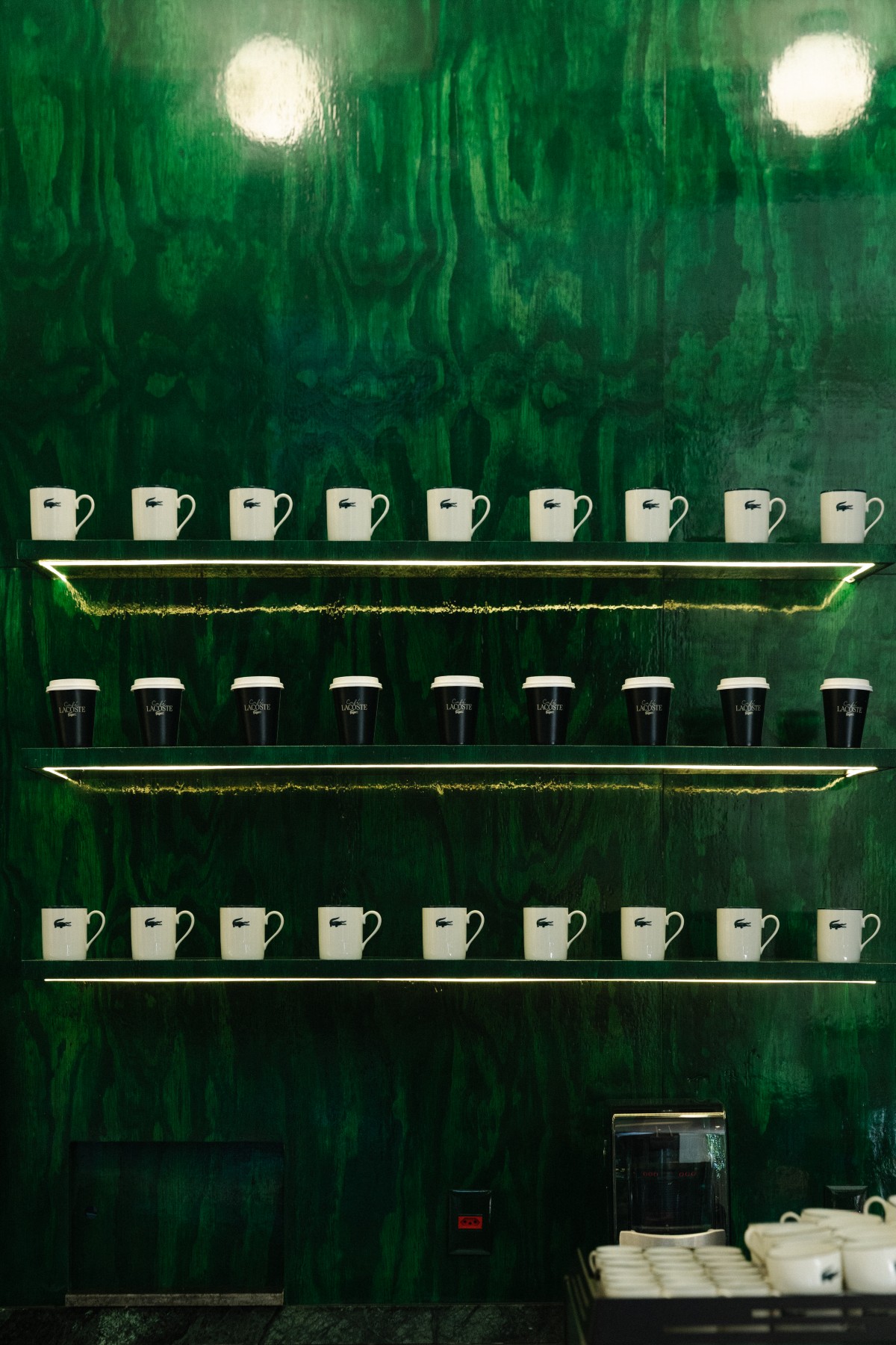 três prateleiras com canecas do café sobre parede verde escura