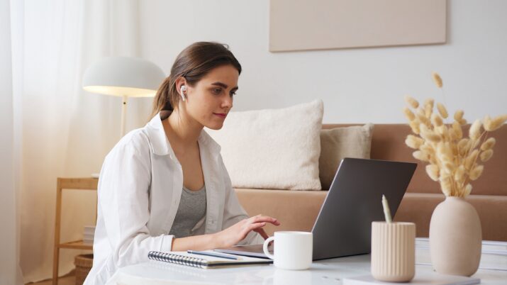 Jovem mulher usando laptop com fones de ouvido para estudar ou trabalhar em casa, cercada por uma decoração aconchegante