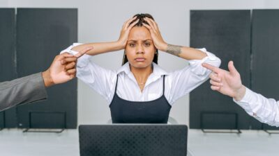 Uma mulher estressada em um ambiente de escritório recebendo culpas de colegas de trabalho, capturando conflito no local de trabalho.