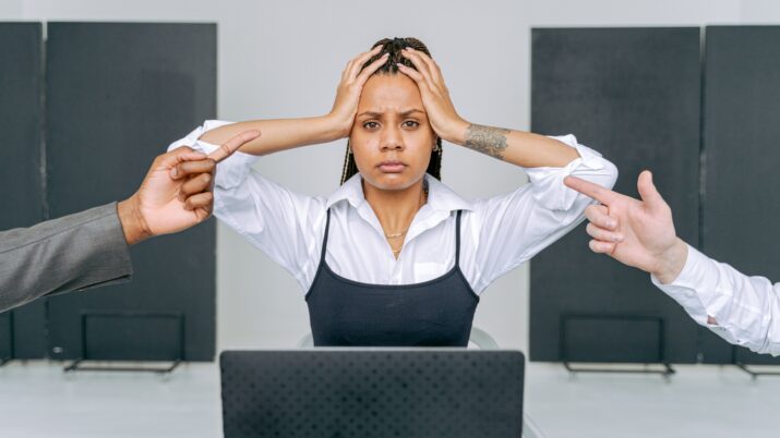 Uma mulher estressada em um ambiente de escritório recebendo culpas de colegas de trabalho, capturando conflito no local de trabalho.