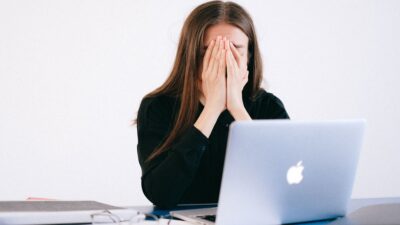 Mulher se sentindo estressada e sobrecarregada em sua mesa enquanto trabalha remotamente em um laptop.