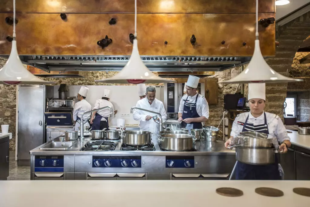 Equipe de cozinheiros em uma cozinha profissional com panelas sobre o fogão e utensílios de inox.