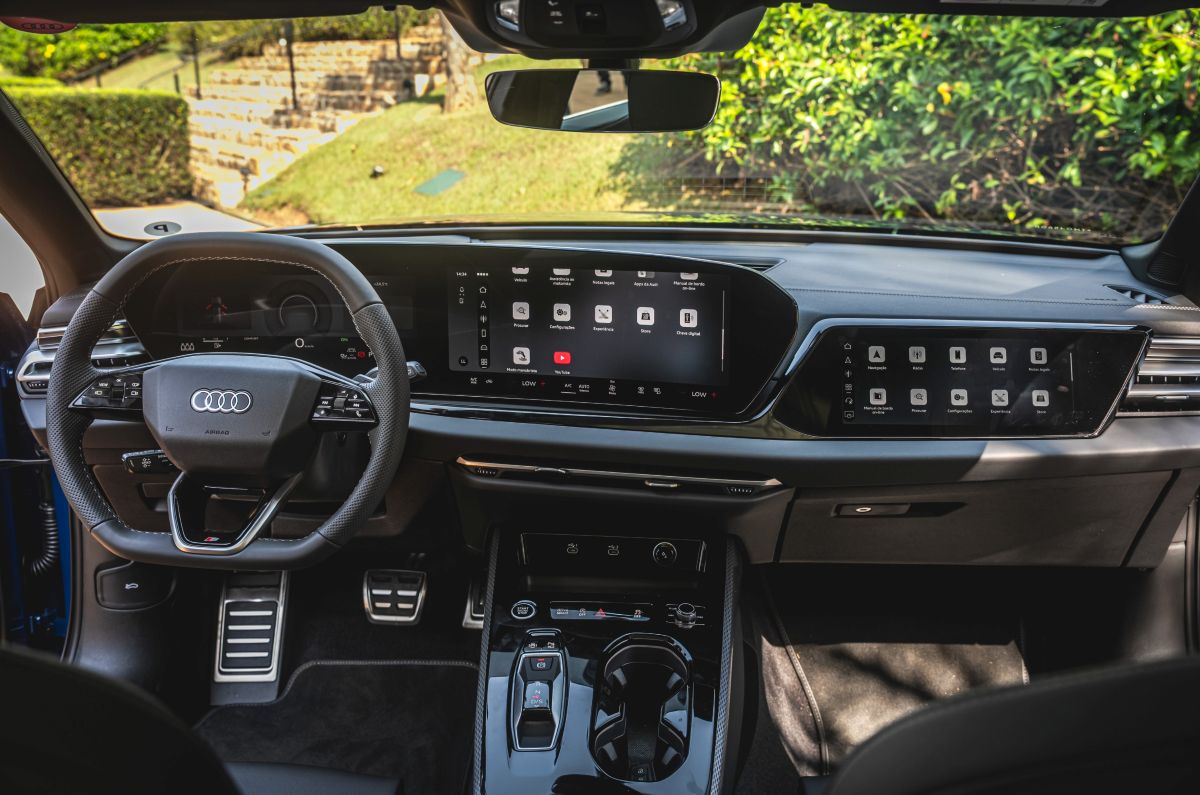 Interior de um carro Audi com volante, painel digital, duas telas centrais e console com seletor de câmbio.