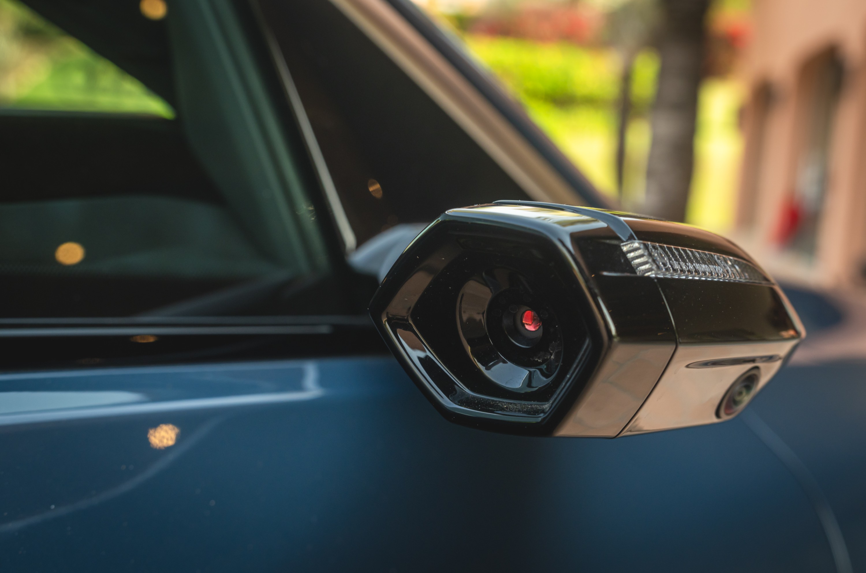 Retrovisor lateral de um carro preto com câmera integrada e seta em LED.