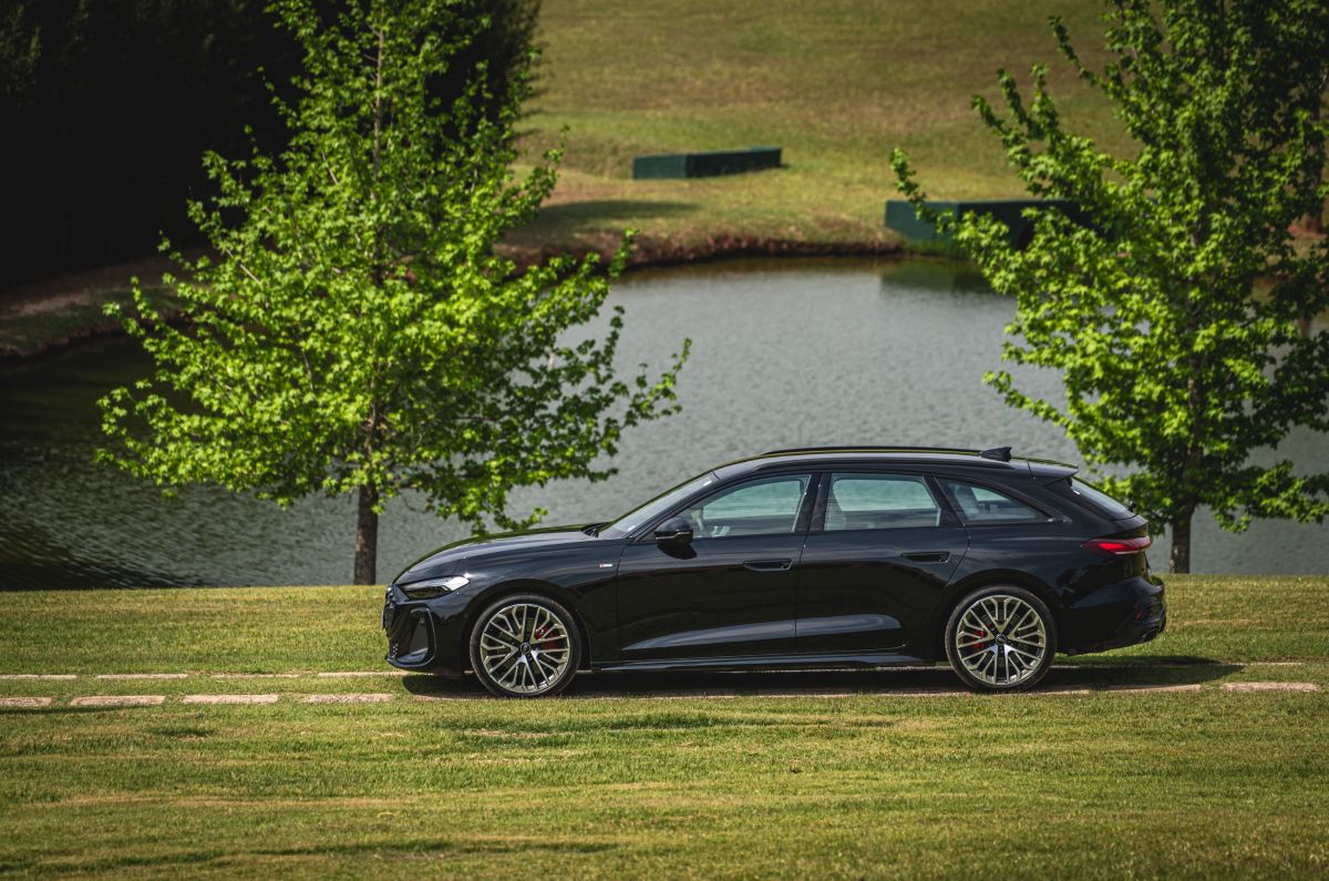 Perua preta da Audi estacionada em gramado ao lado de um lago, com árvores ao fundo.