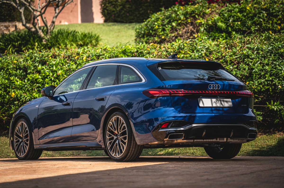 Perua Audi A5 azul vista de traseira e lateral, estacionada em área externa com vegetação ao fundo.