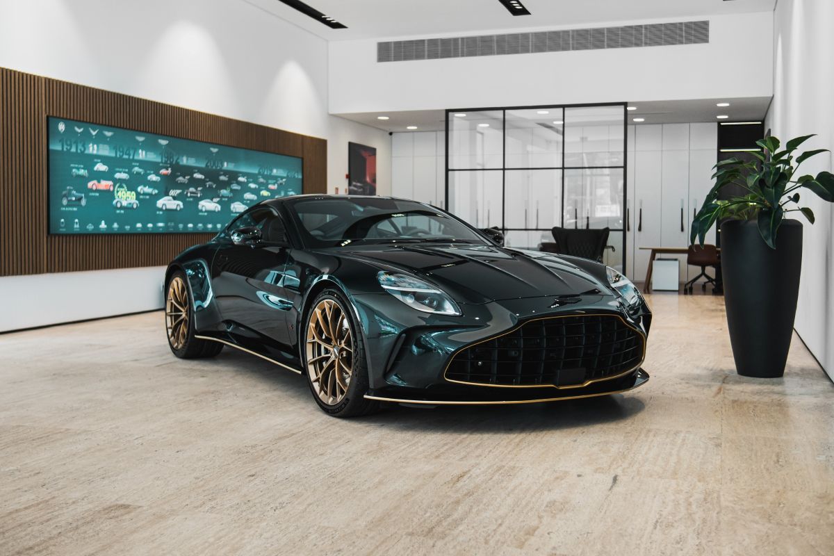 Carro esportivo preto com detalhes dourados exposto em uma sala moderna e iluminada.
