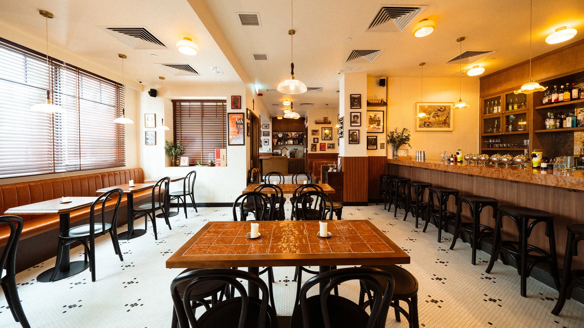 Interior de um bar vazio com mesas de madeira, cadeiras pretas, balcão com banquetas e prateleiras de bebidas.