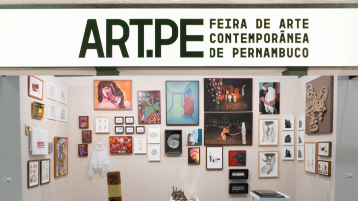 Estande da Art.PE com várias obras emolduradas e peças tridimensionais expostas em uma parede branca.