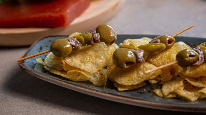 Espetinhos com azeitonas sobre batatas fritas em um prato oval.