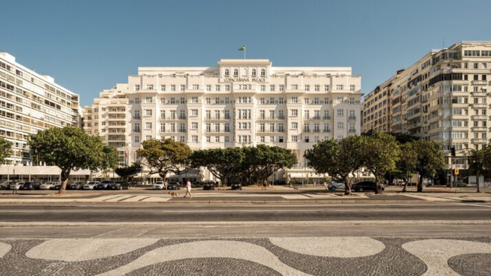 Fachada do Copacabana Palace vista da avenida, com prédios ao lado, árvores na calçada e céu limpo.