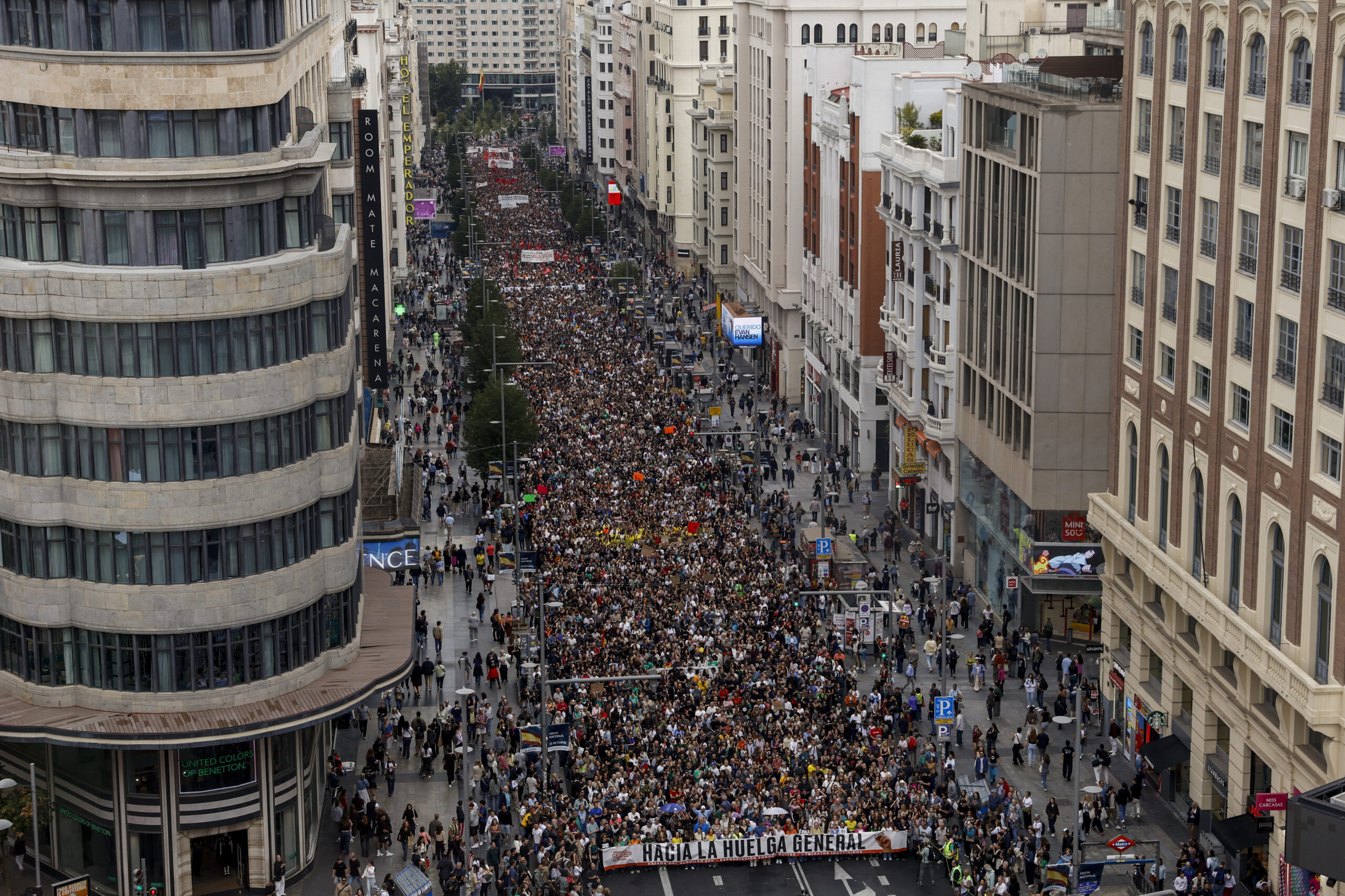 Multidão ocupa uma avenida entre prédios altos, com faixas e cartazes durante uma manifestação.