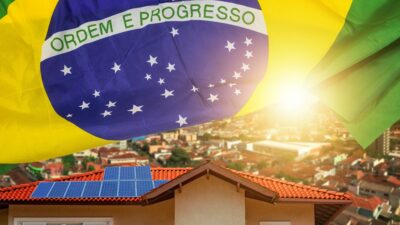Foto de stock de Painel de uma casa em primeiro plano com bandeira do Brasil ao fundo. No horizonte, uma cidade ao pôr do sol. ID Criativo: 1269507946