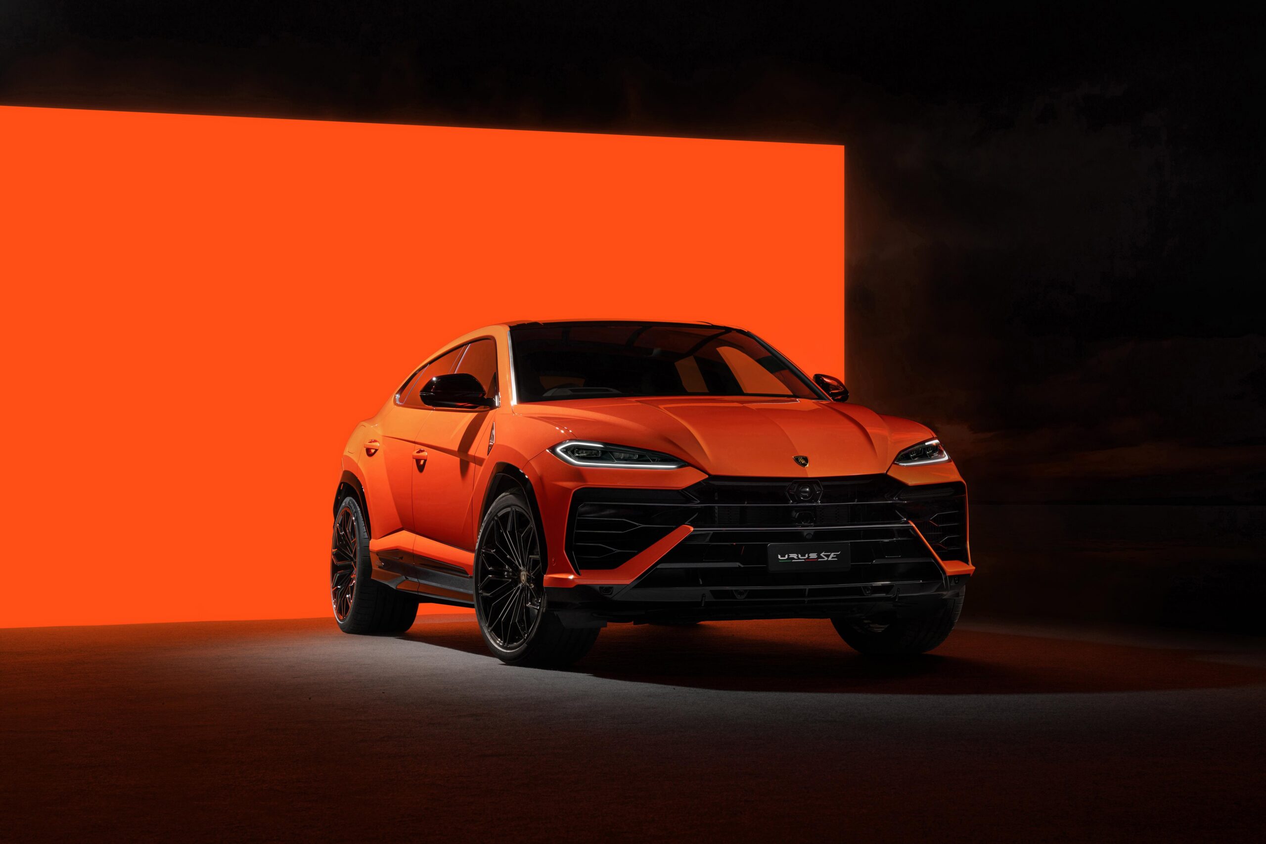 SUV laranja em estúdio, com frente preta, faróis afilados e fundo iluminado em laranja e preto.