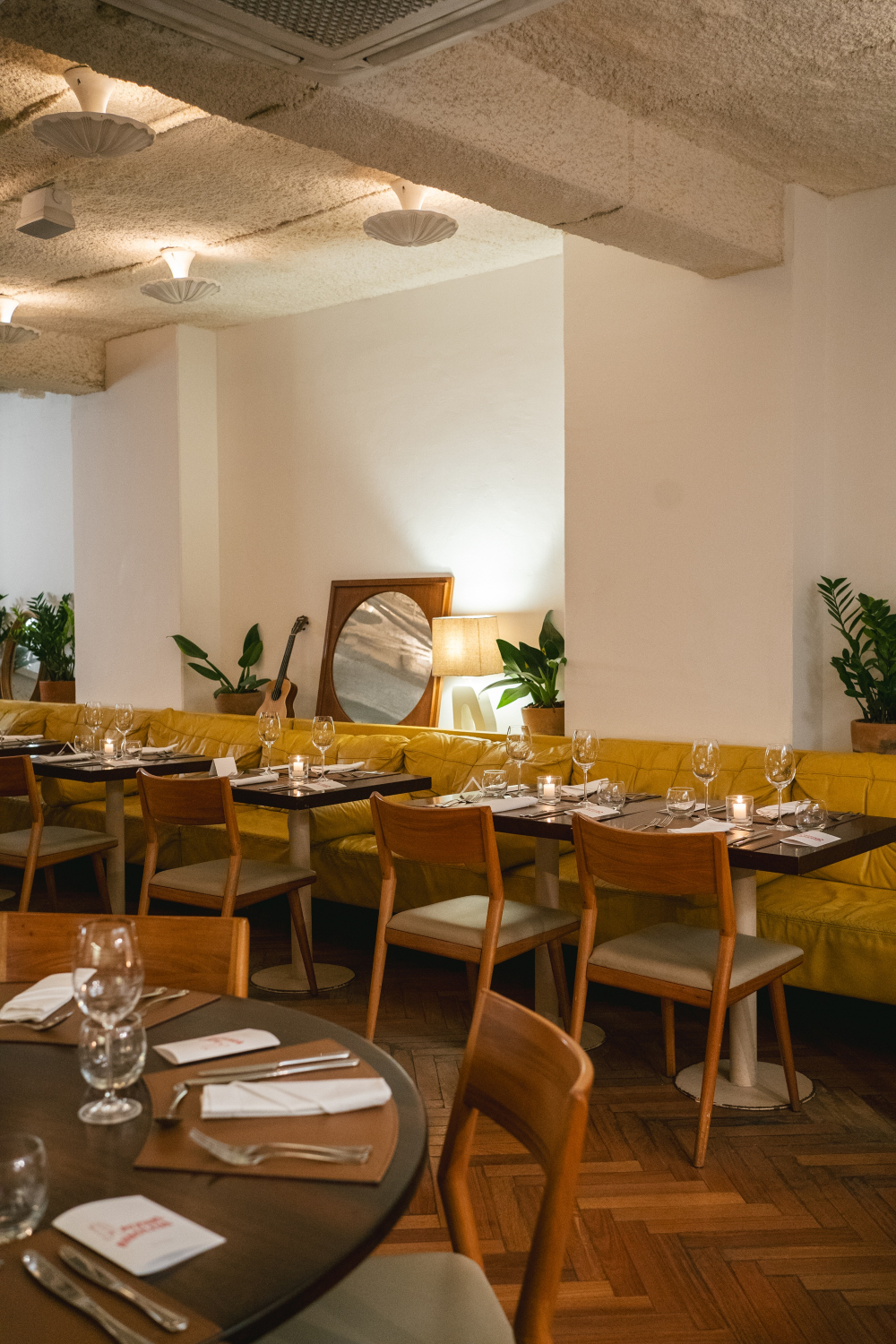 Salão de restaurante com mesas postas, cadeiras de madeira, sofá amarelo e iluminação suave.