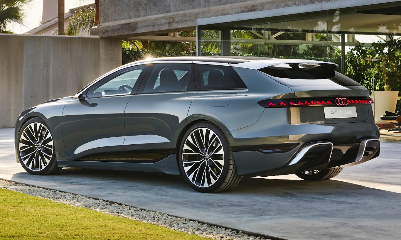 Perua Audi cinza vista de traseira lateral, estacionada em uma garagem moderna com vidro e jardim ao fundo.