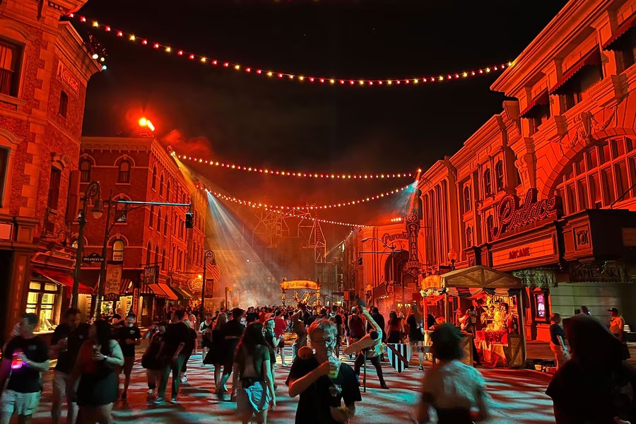 Rua movimentada à noite com prédios iluminados em vermelho, luzes penduradas e pessoas caminhando.