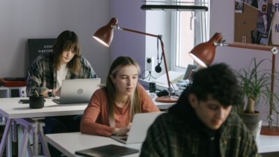 Três jovens profissionais trabalhando em mesas em um escritório moderno com laptops e luminárias