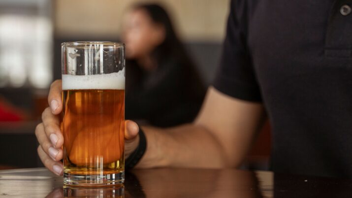 Close-up de uma mão adulta segurando um copo de cerveja com espuma em um ambiente informal de pub