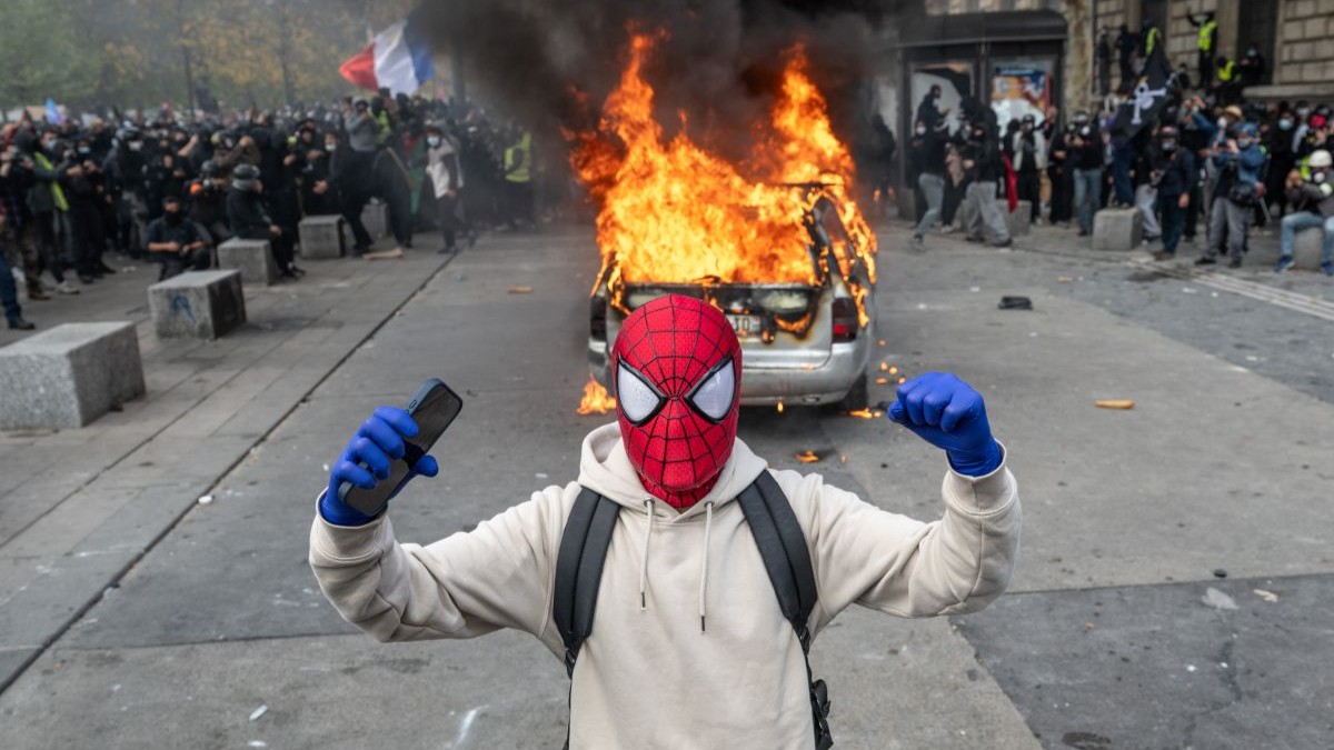 Um manifestante vestido de Homem-Aranha faz gestos enquanto um carro queima durante uma manifestação na Place de la République, em 17 de outubro de 2026, em Paris, França. "Coletes Amarelos" se uniram a manifestantes de escolas francesas para um fim de semana de mobilização.